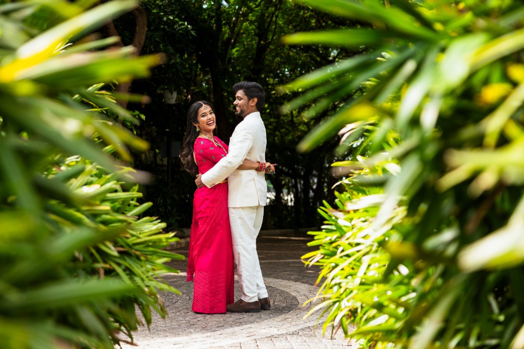 Pre-Wedding — Couple framed by tropical leaves, laughing in garden