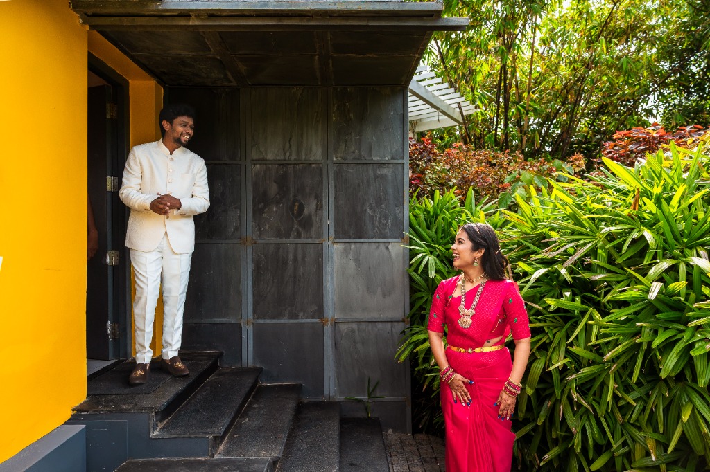 Pre-Wedding — Groom on steps, bride looking up from garden — yellow wall backdrop