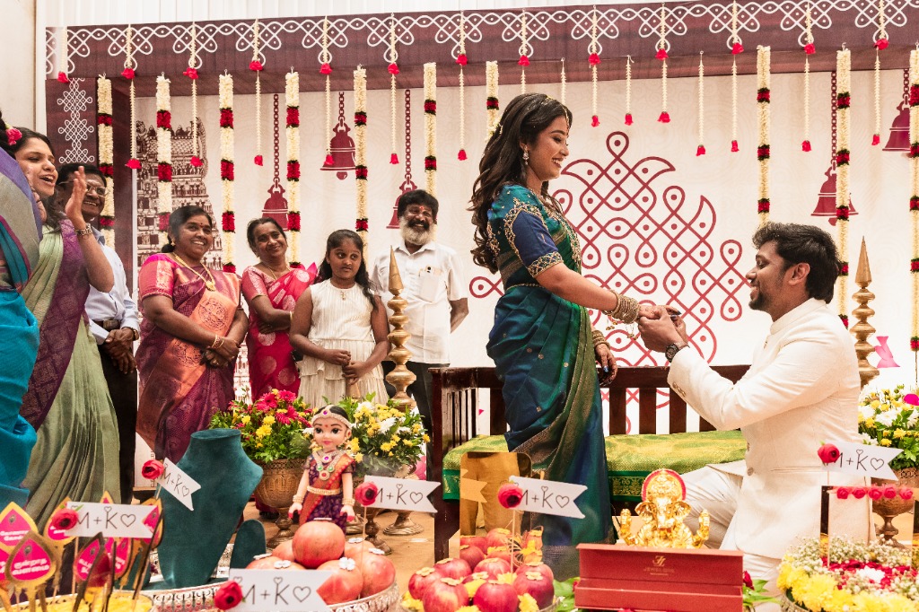Engagement — Groom placing ring on stage with family watching