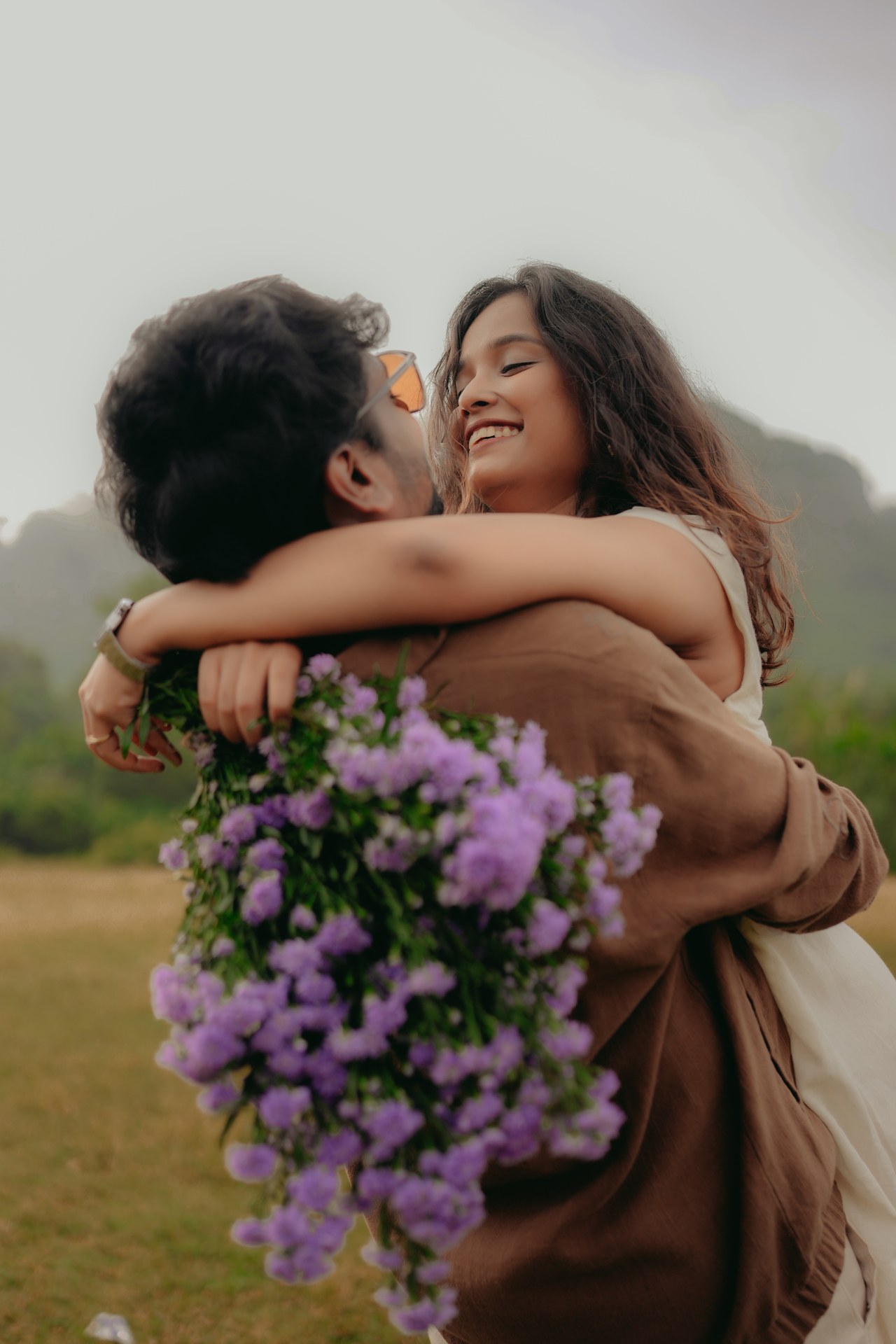 Pre-Wedding — Couple holding purple flowers together, close-up of hands